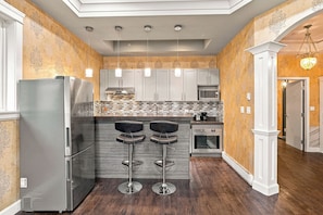 A modern kitchen with stainless steel appliances, a central island with bar stools, and decorative lighting. - Tranquil 2-bedroom house in charming Surrey perfect for relaxing stays (Surrey)
