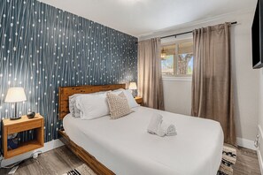 A neatly made bed with white linens and two pillows, a bedside table with a lamp, and a window with curtains. - Large Modern Retreat, 6BR, Game + Movie Room, Firepit, Private Fenced Backyard (Westminster)