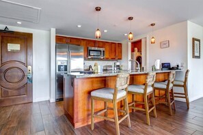 A modern kitchen with wooden cabinets, stainless steel appliances, and a central island with bar stools. - Honua Kai Resort - 4 BR (2 condos), Sleeps 8 (Lahaina)