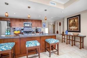 A modern kitchen with wooden cabinets, a central island with bar stools, and pendant lighting. - Honua Kai Resort - 4 BR (2 condos), Sleeps 8 (Lahaina)