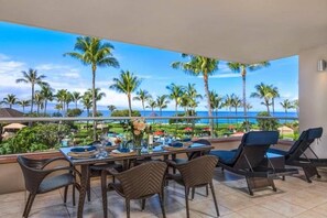 A dining area with a view of the ocean and palm trees, furnished with chairs and a table. - Honua Kai Resort - 4 BR (2 condos), Sleeps 8 (Lahaina)