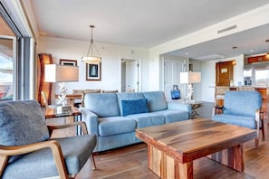A modern living room with a sofa, chairs, a coffee table, and a kitchen area in the background. - Honua Kai Resort - 4 BR (2 condos), Sleeps 8 (Lahaina)