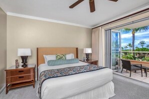 A hotel room with a large bed, two bedside tables, a desk, and a balcony with a view of palm trees. - Honua Kai Resort - 4 BR (2 condos), Sleeps 8 (Lahaina)