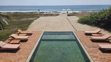 A pool area with lounge chairs and a view of the beach.