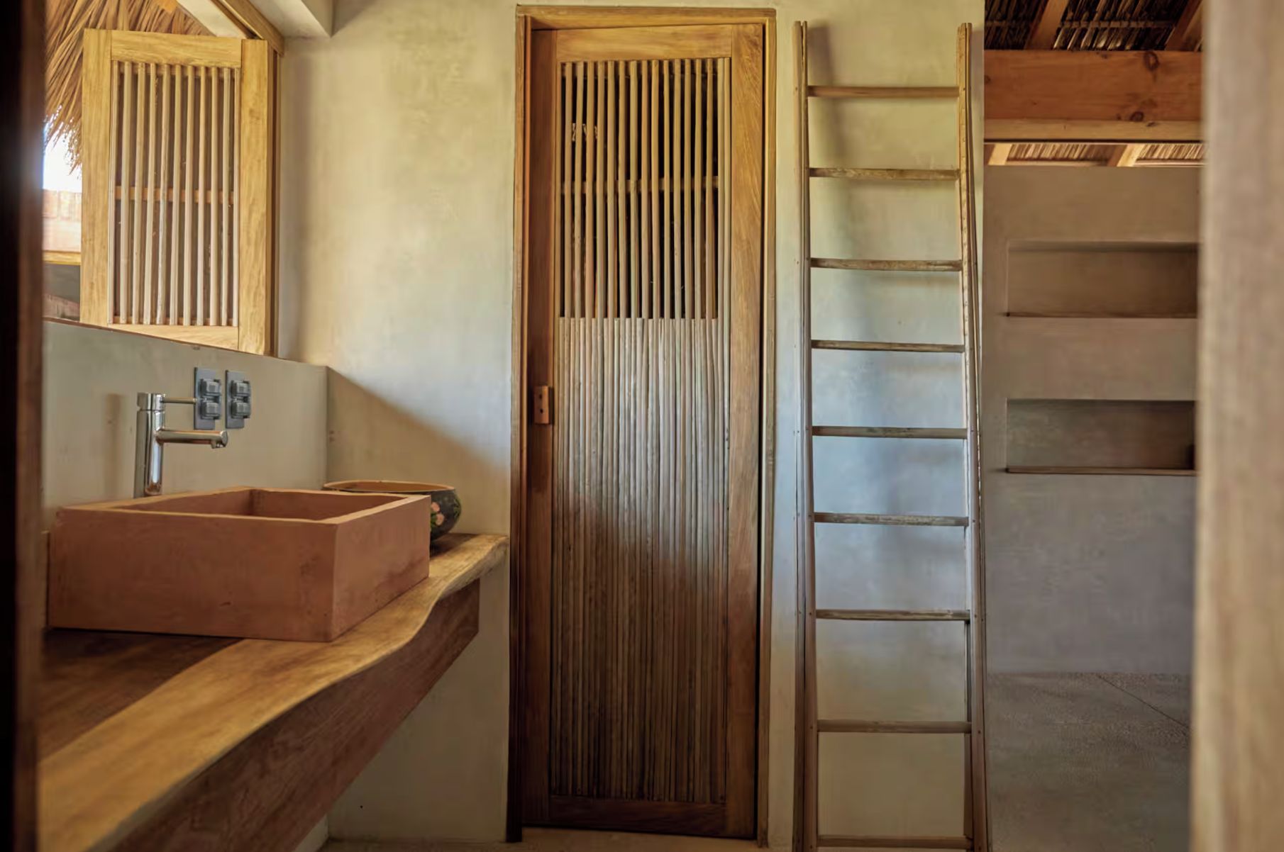 A bathroom with a wooden sink, a vertical wooden door, and a wooden ladder.