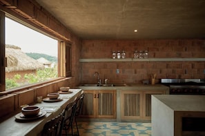 A kitchen with wooden cabinets, a sink, and a window overlooking a thatched-roof structure. - Bespoke Oceanfront Home in Oaxaca (San Isidro Llano Grande)