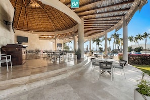 A covered outdoor area with a thatched roof, seating arrangements, and a poolside view. - Villa 78 | 2 Private Pools + Beach Club Access (Cruz de Huanacaxtle)