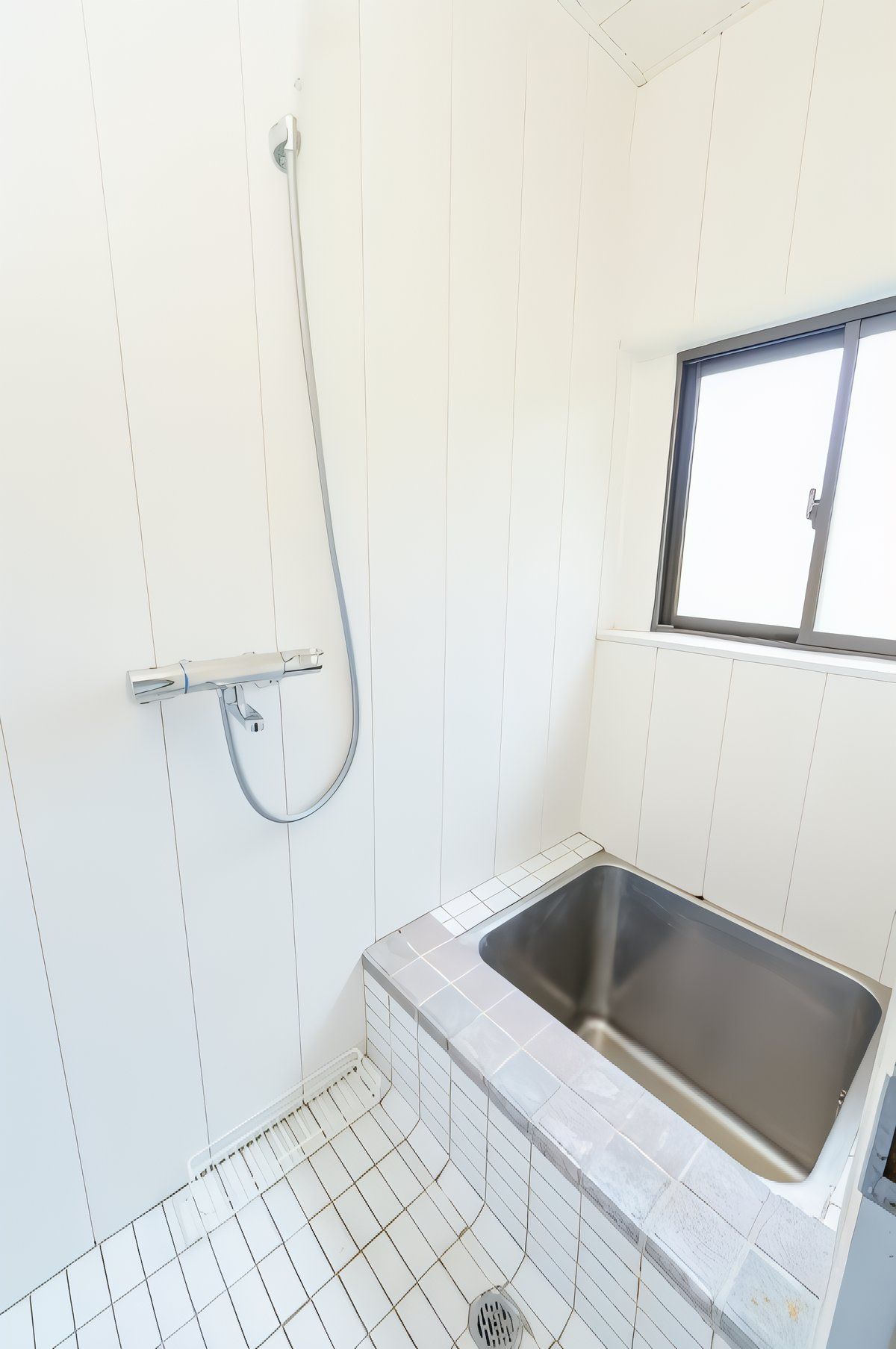 A small bathroom with a shower, a window, and a sink.