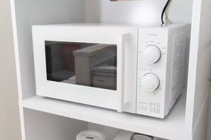 Eine weiße Mikrowelle mit digitaler Anzeige und Bedienelementen an der rechten Seite, auf einem weißen Regal platziert.