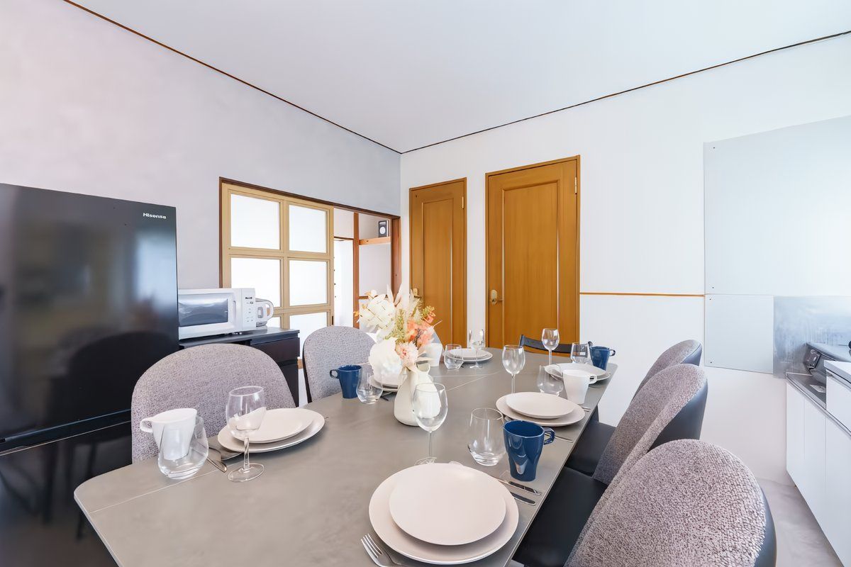A modern dining area with a long table set for six, equipped with plates, glasses, and cutlery.