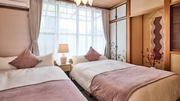 A hotel room with two beds, a window with curtains, a lamp, and a decorative wall panel.