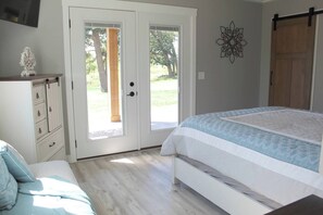Ein Schlafzimmer mit Bett, Kommode, einer zur Außenwelt führenden Tür und einem an der Wand befestigten Dekorationsobjekt.