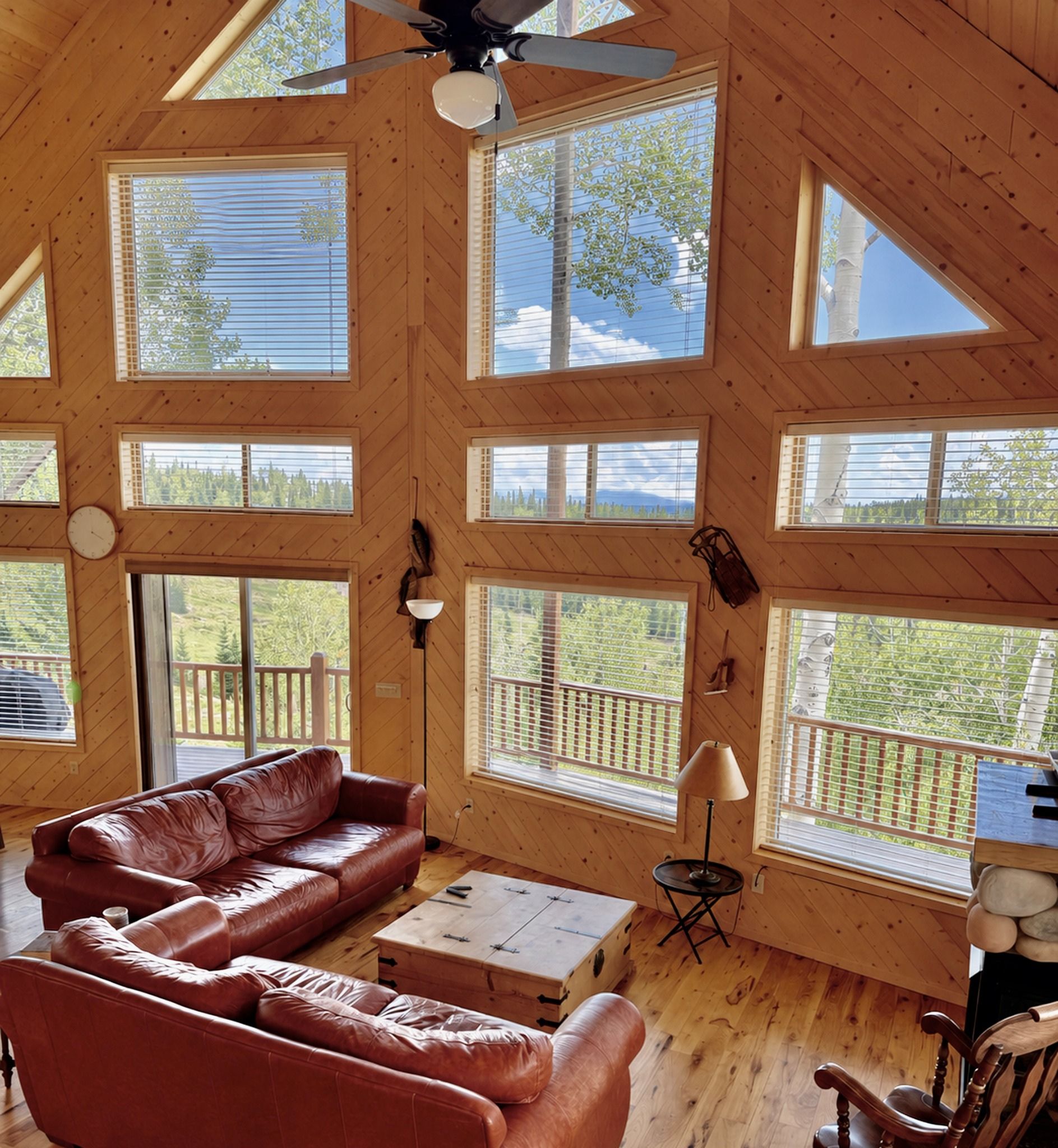 A spacious loft with a high ceiling, large windows, a leather sofa, a small table, and a wooden chair.