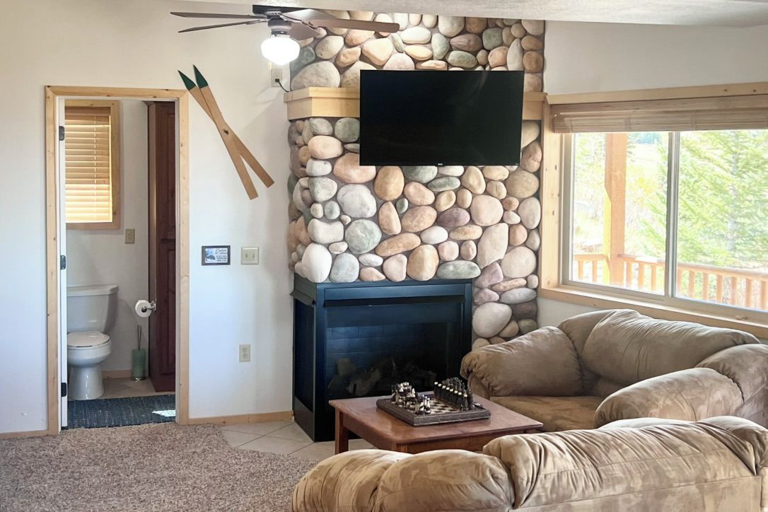 Una sala de estar con pared de piedra, chimenea, televisor y sofá.