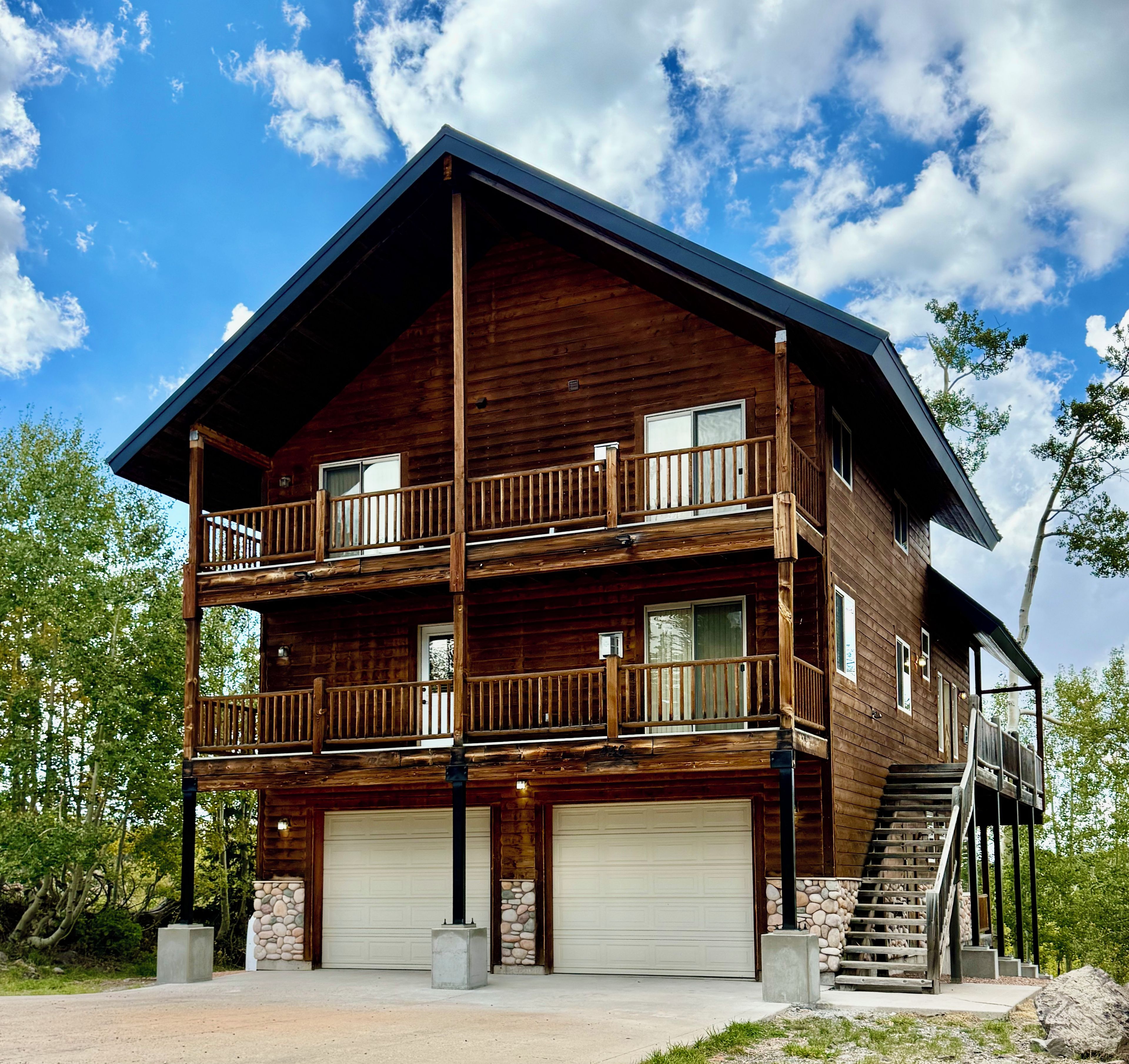 A two-story log cabin with a balcony, a garage, and a staircase leading to an upper level.