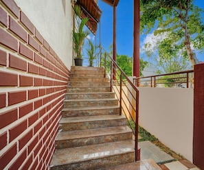 A staircase with a brick wall on one side and a metal railing on the other, leading to a covered area with a potted plant. - Classic Pool Villa Home Stay (Mysore)