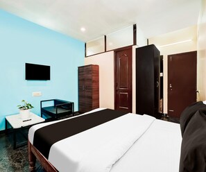 A hotel room with a bed, a desk with a chair, a potted plant, and a wardrobe. - Classic Pool Villa Home Stay (Mysore)