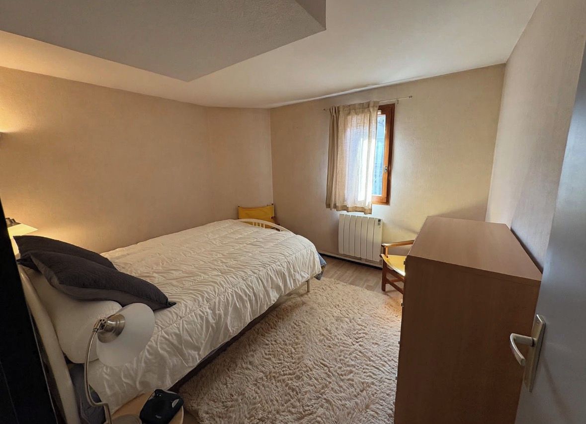 Un dormitorio con cama, escritorio, silla, radiador y ventana con cortinas.