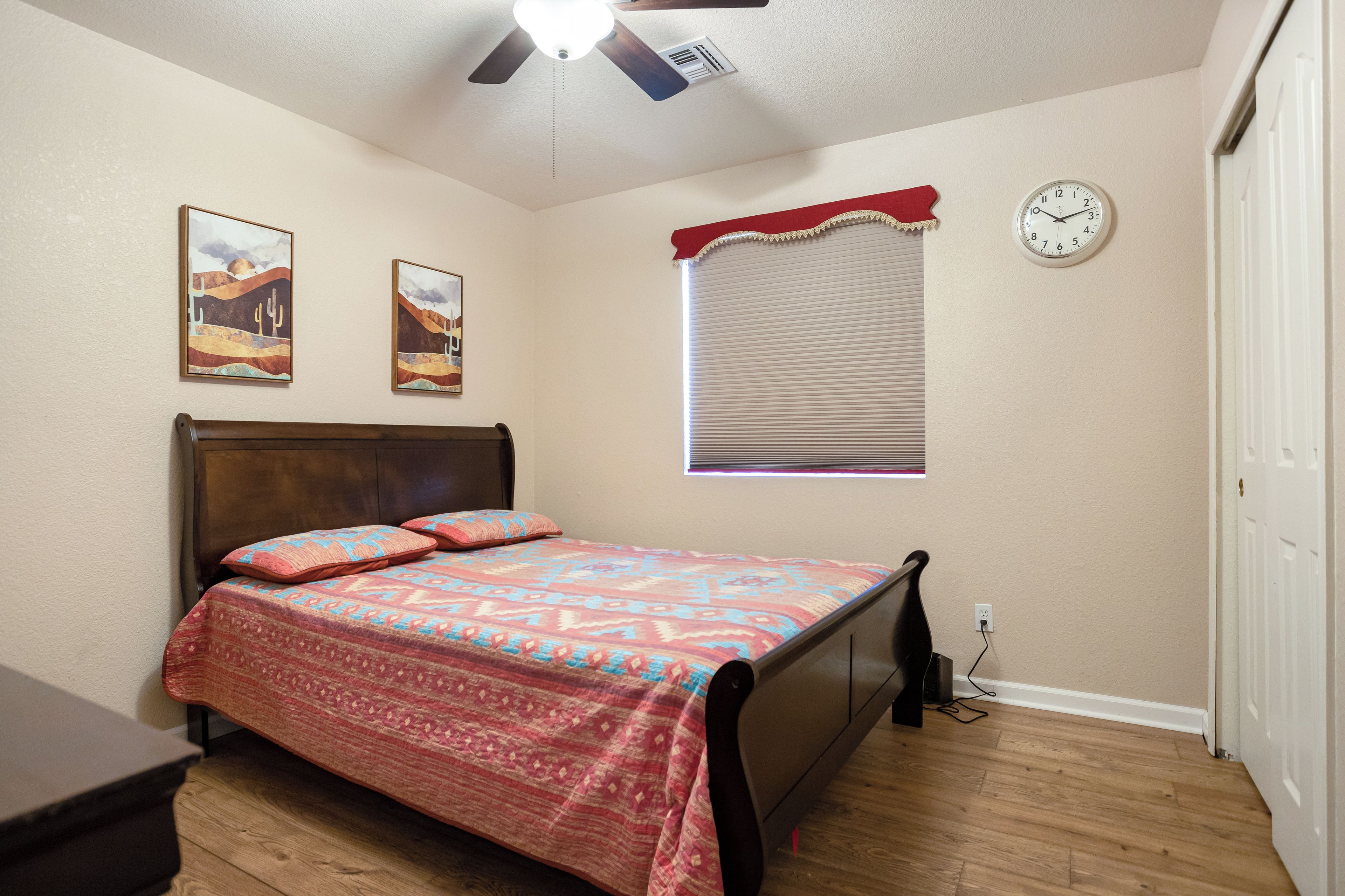 Une chambre à coucher avec un lit, un ventilateur de plafond, une horloge et une fenêtre avec des stores.
