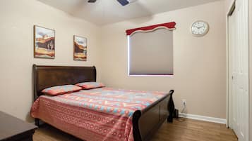 Une chambre à coucher avec un lit, un ventilateur de plafond, une horloge et une fenêtre avec des stores.