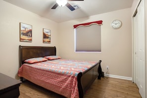 Una camera da letto con un letto, una ventola a soffitto, una sveglia e una finestra con tende.