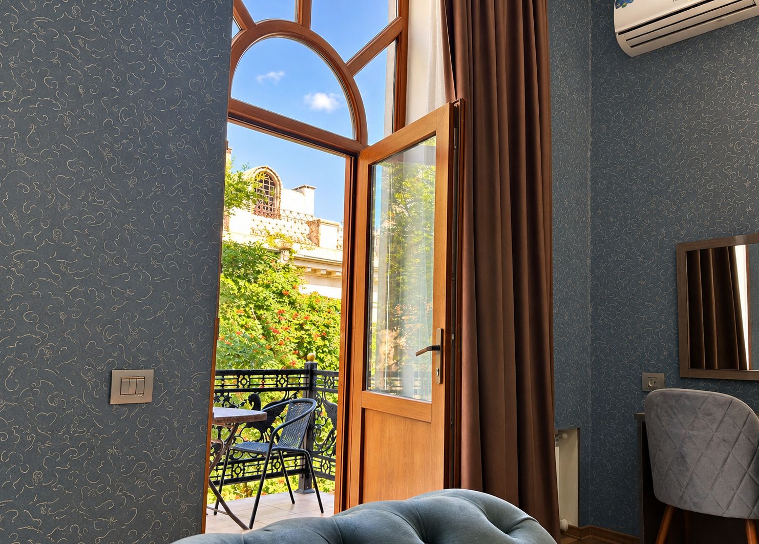 Una habitación con un ventanal grande, una cama, una silla y una mesa con sillas afuera.