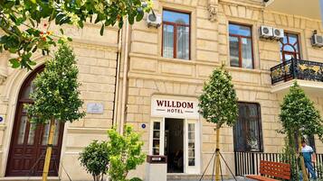 L’entrée d’un hôtel, agrémentée d’une enseigne indiquant « HÔTEL WILDOM », est entourée d’un aménagement paysager soigné et présente un style architectural traditionnel.