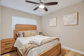 A bedroom with a wooden bed, a nightstand, a ceiling fan, and two wall art pieces. - Casa Anduro 5BR Pool & Spa Near San Diego (Chula Vista)