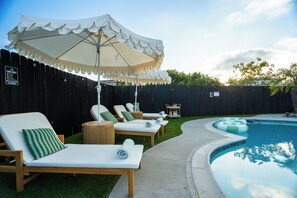 Ein Garten mit Swimmingpool, Liegestühlen und einem überdachten Bereich mit Sonnenschirm.
