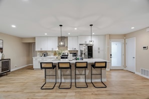 Una cocina moderna con armarios blancos, una isla central con taburetes altos e iluminación colgante.