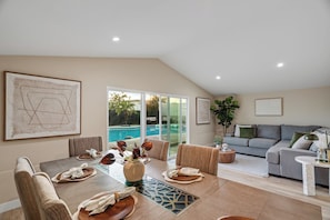 A spacious living room with a dining area, a gray sofa, and a view of a swimming pool. - Casa Anduro 5BR Pool & Spa Near San Diego (Chula Vista)