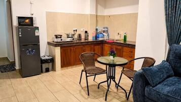 A compact kitchen with a refrigerator, stove, and dining area with chairs.