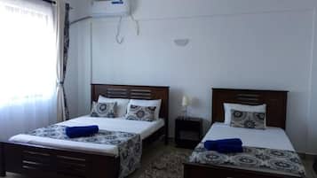 A hotel room with two beds, a ceiling fan, an air conditioning unit, and a small bedside table with a lamp.
