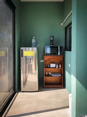 A compact kitchenette with a stainless steel refrigerator, a microwave, and a wooden shelf with various items. - The Amate de Monticello (Los Planes de Renderos)