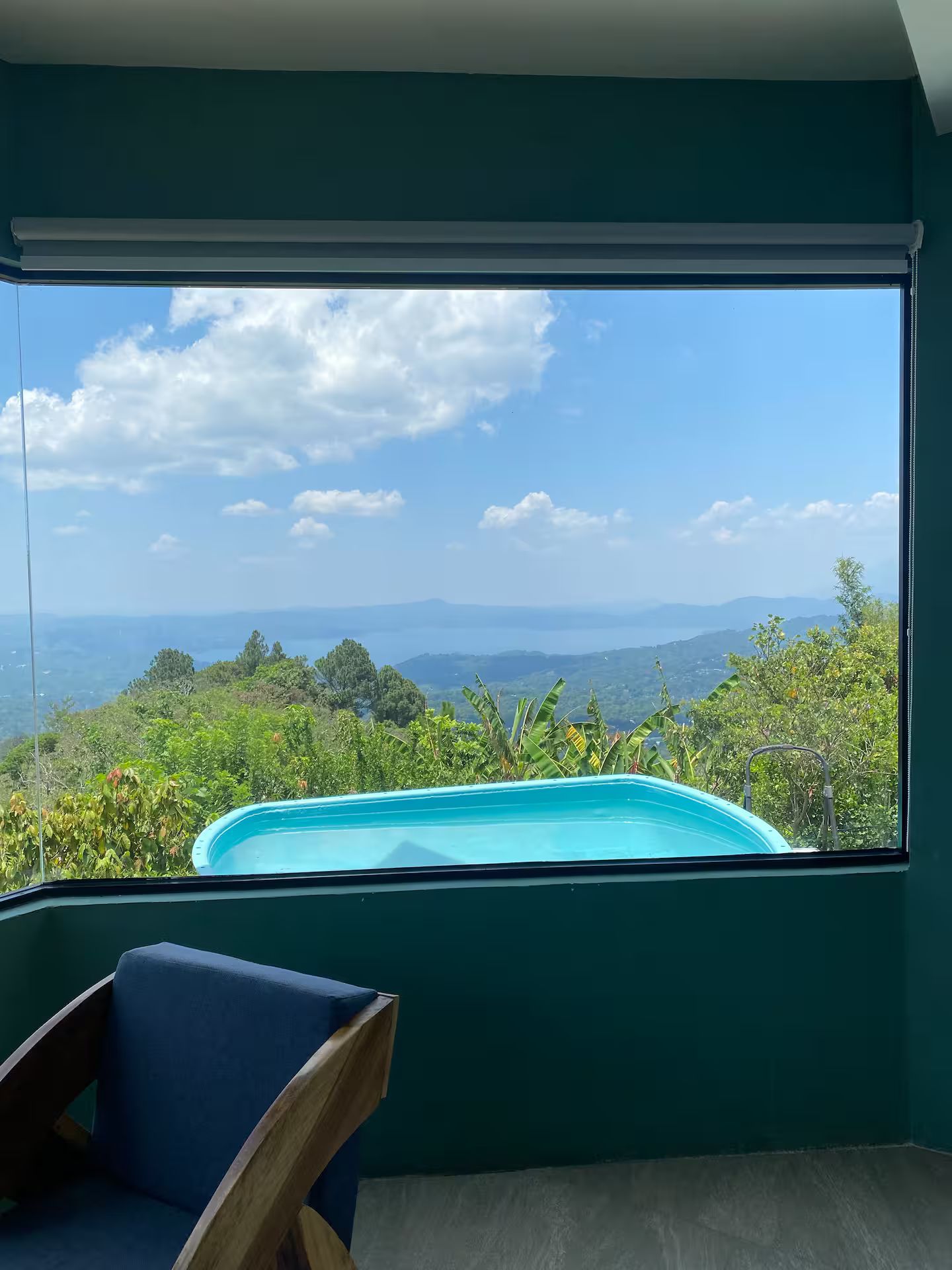 A room with a large window overlooking a mountainous landscape and a swimming pool.