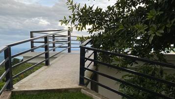 A concrete pathway with metal railings leading to a grassy area, surrounded by foliage.
