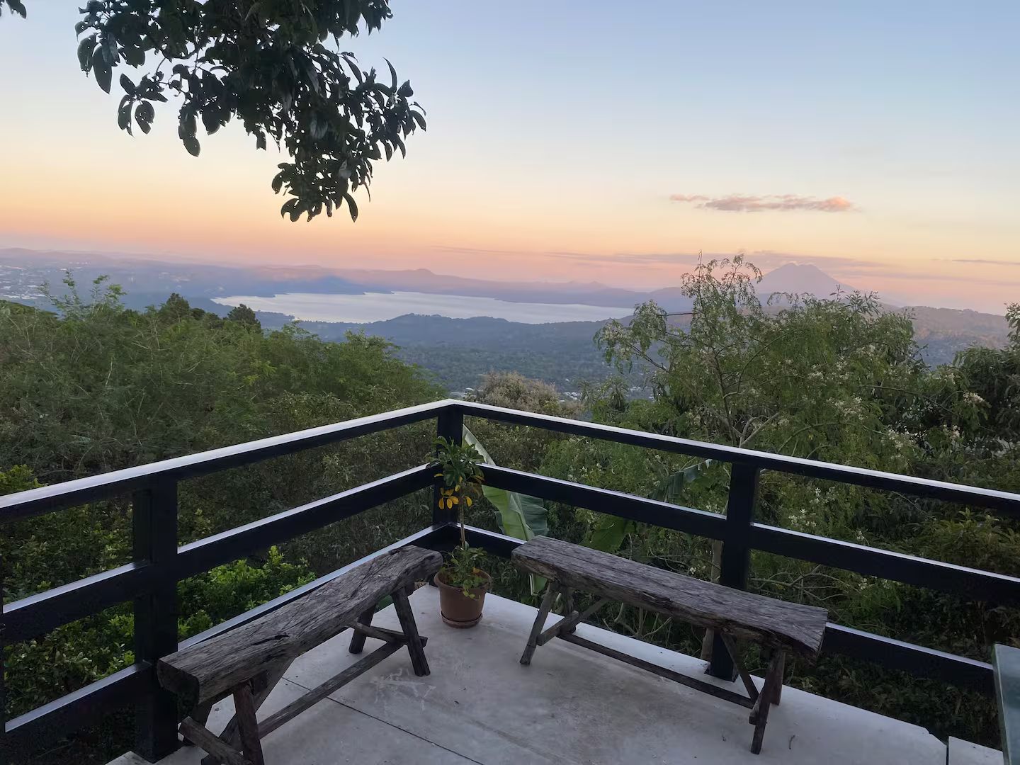 A wooden bench and a potted plant on a balcony with a view of a mountain and a body of water.