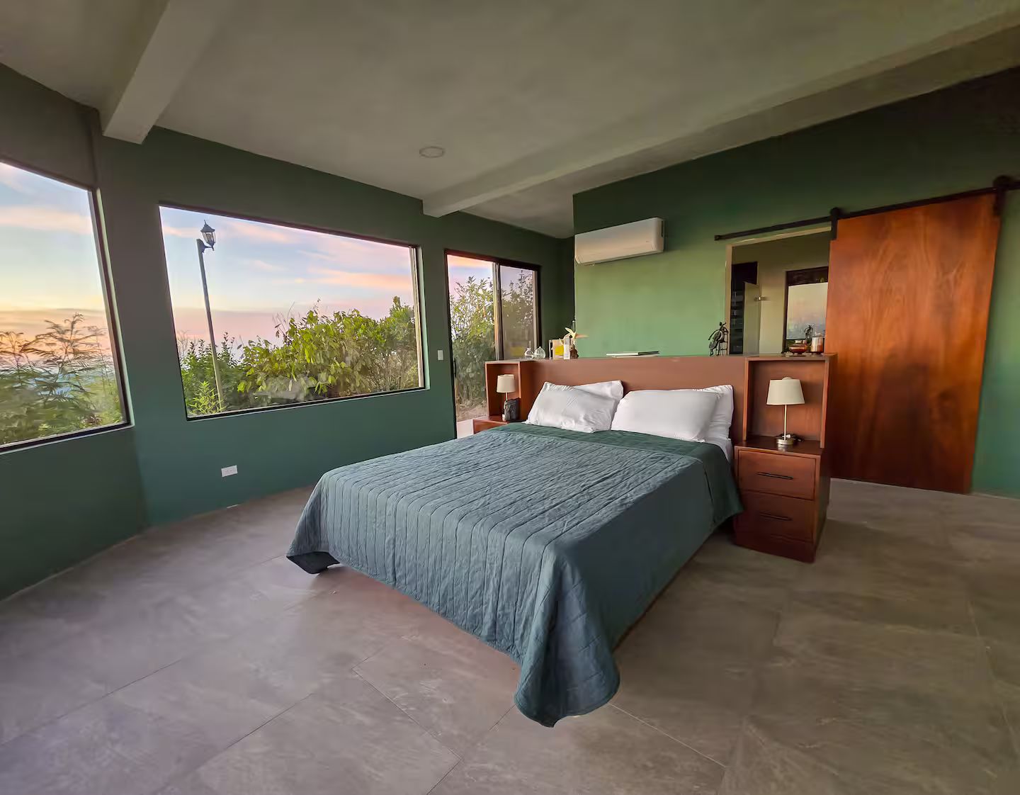 A bedroom with a bed, nightstands, a mirror, and large windows.