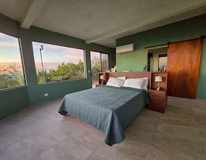 A bedroom with a bed, nightstands, a mirror, and large windows. - The Amate de Monticello (Los Planes de Renderos)