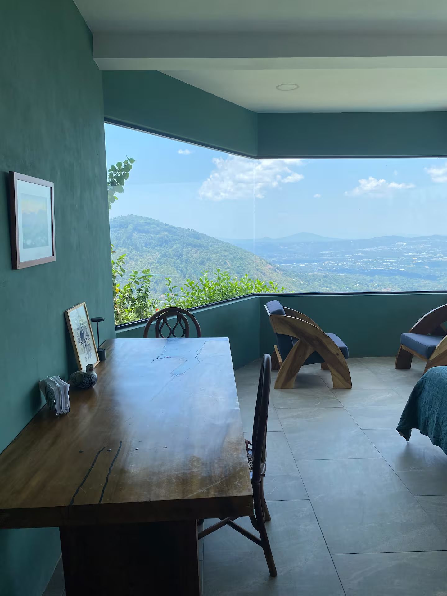 A room with a wooden table, chairs, and a large window offering a view of a mountainous landscape.
