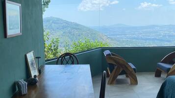 A room with a wooden table, chairs, and a large window offering a view of a mountainous landscape.