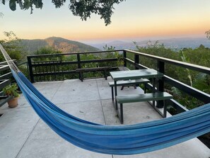 A hammock on a balcony with a view of hills and a sunset. - The Amate de Monticello (Los Planes de Renderos)