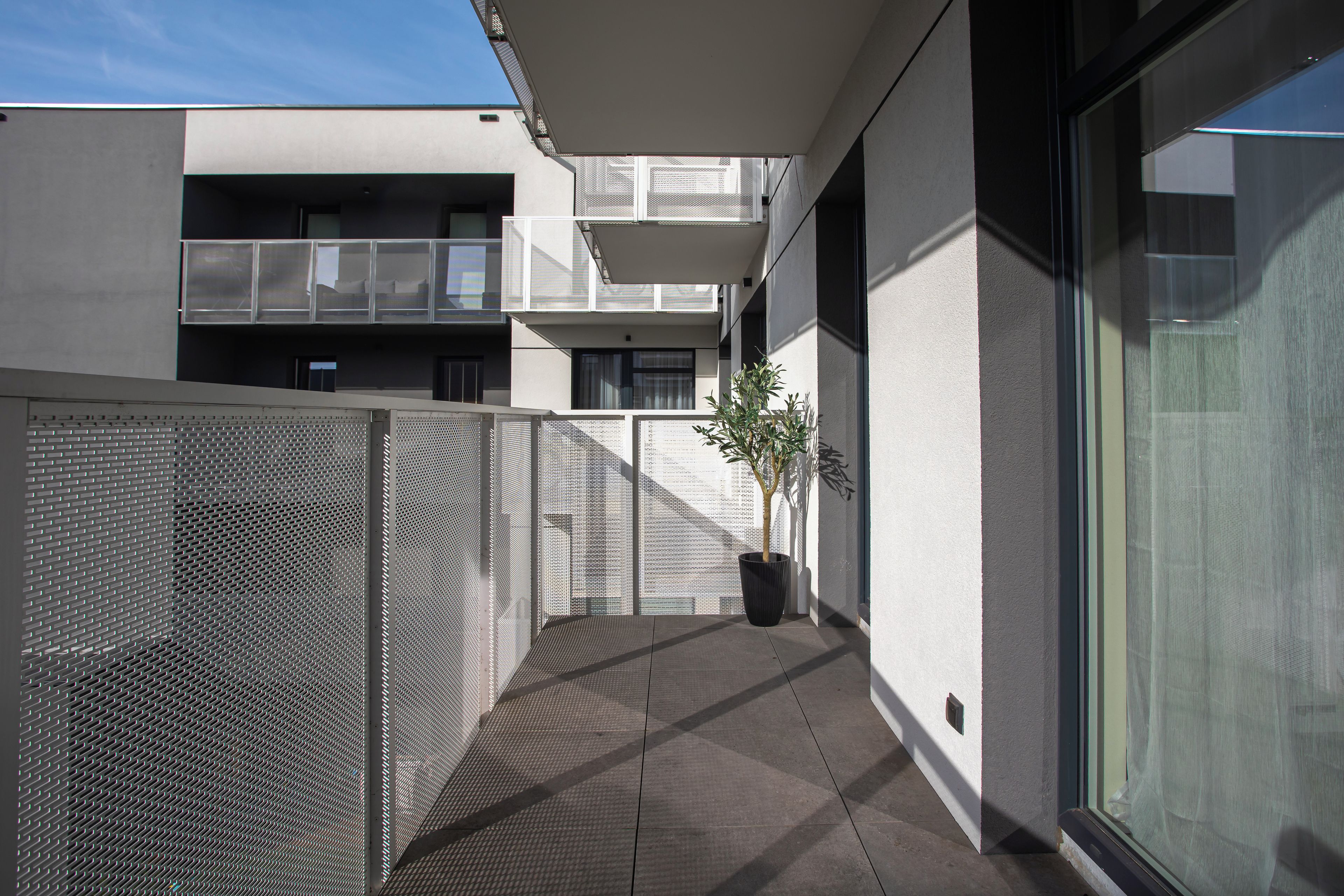 Un bâtiment moderne doté d’un balcon, d’un pot de fleurs et d’une clôture en treillis métallique.