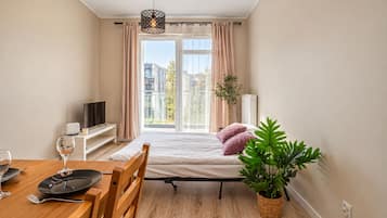 A modern bedroom with a bed, a TV, a dining table with chairs, and a potted plant.