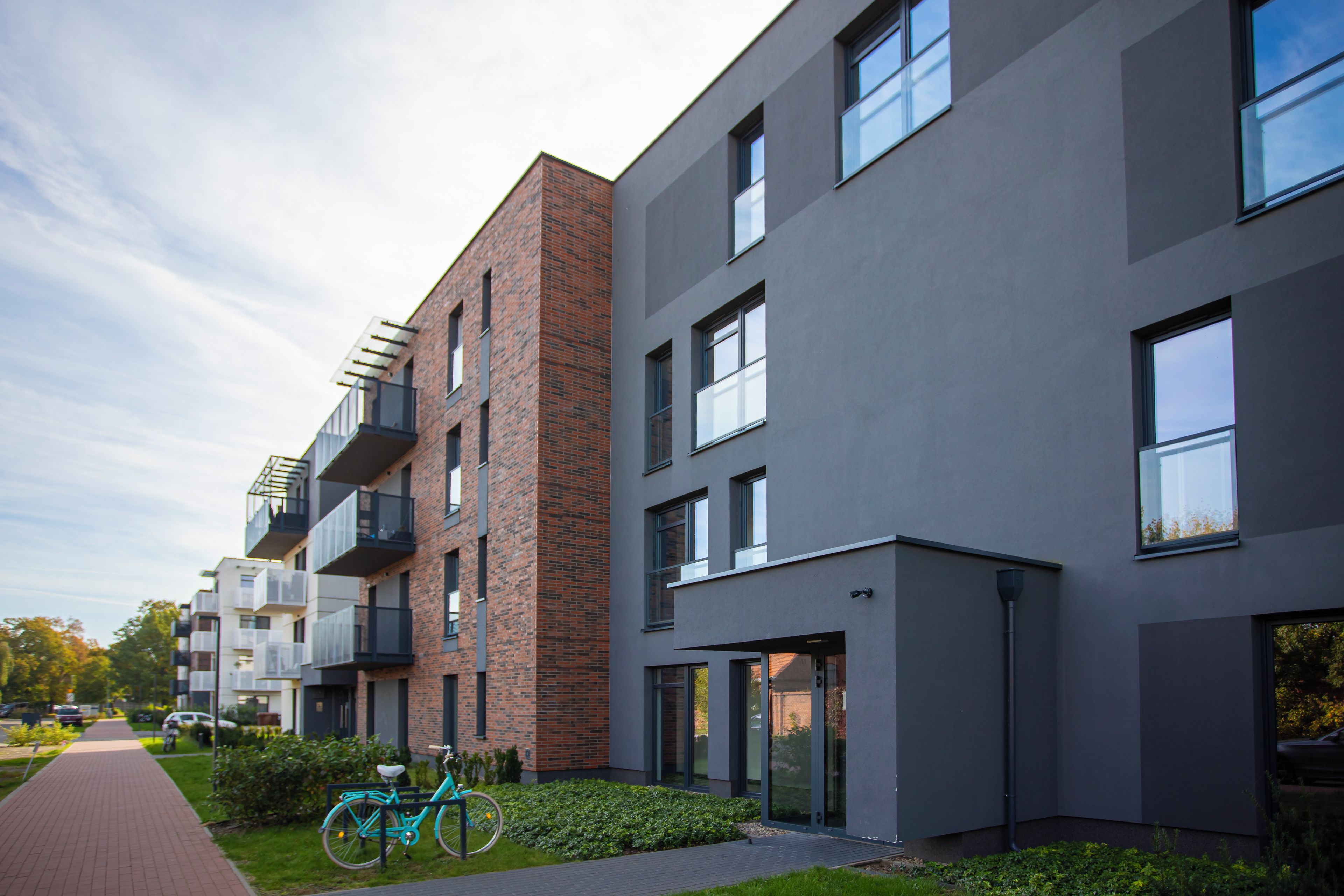 A modern apartment building with balconies, large windows, and a paved walkway.
