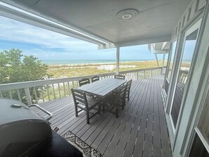 A covered outdoor deck with a table and chairs, overlooking a beach. - Beachfront Home on Anna Maria Island! (Anna Maria Island)