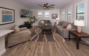 Una sala de estar con sofá, sillón, mesa de centro y ventilador de techo.