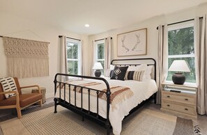 A bedroom with a bed, bedside tables, a chair, and a window with curtains. - Fir Haven Farmhouse - Stylish 3BR Escape on Whidbey (Freeland)