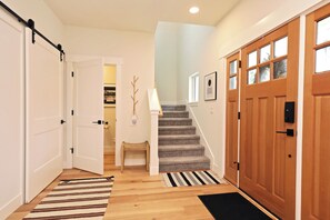 A hallway with a wooden floor, a striped rug, a bench, a staircase, and a wooden door with glass panels. - Fir Haven Farmhouse - Stylish 3BR Escape on Whidbey (Freeland)