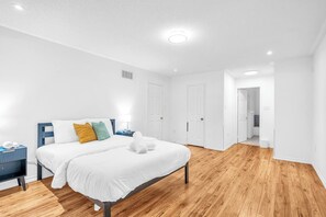 A modern hotel room with a wooden floor, a bed with white bedding, a nightstand, and a lamp. - Minutes to Thermëa Spa, Hwy 401, GO Train & Golf (Ajax)
